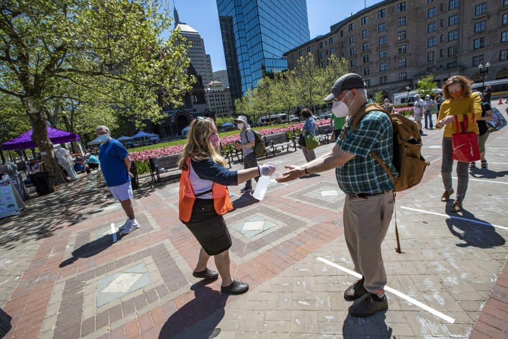 Edith Murnane, executive director of the Mass Farmers Markets, sprays hand sanitizer on the hands of everyone standing in line to enter the Copley Square Farmers Market. (Jesse Costa/WBUR)