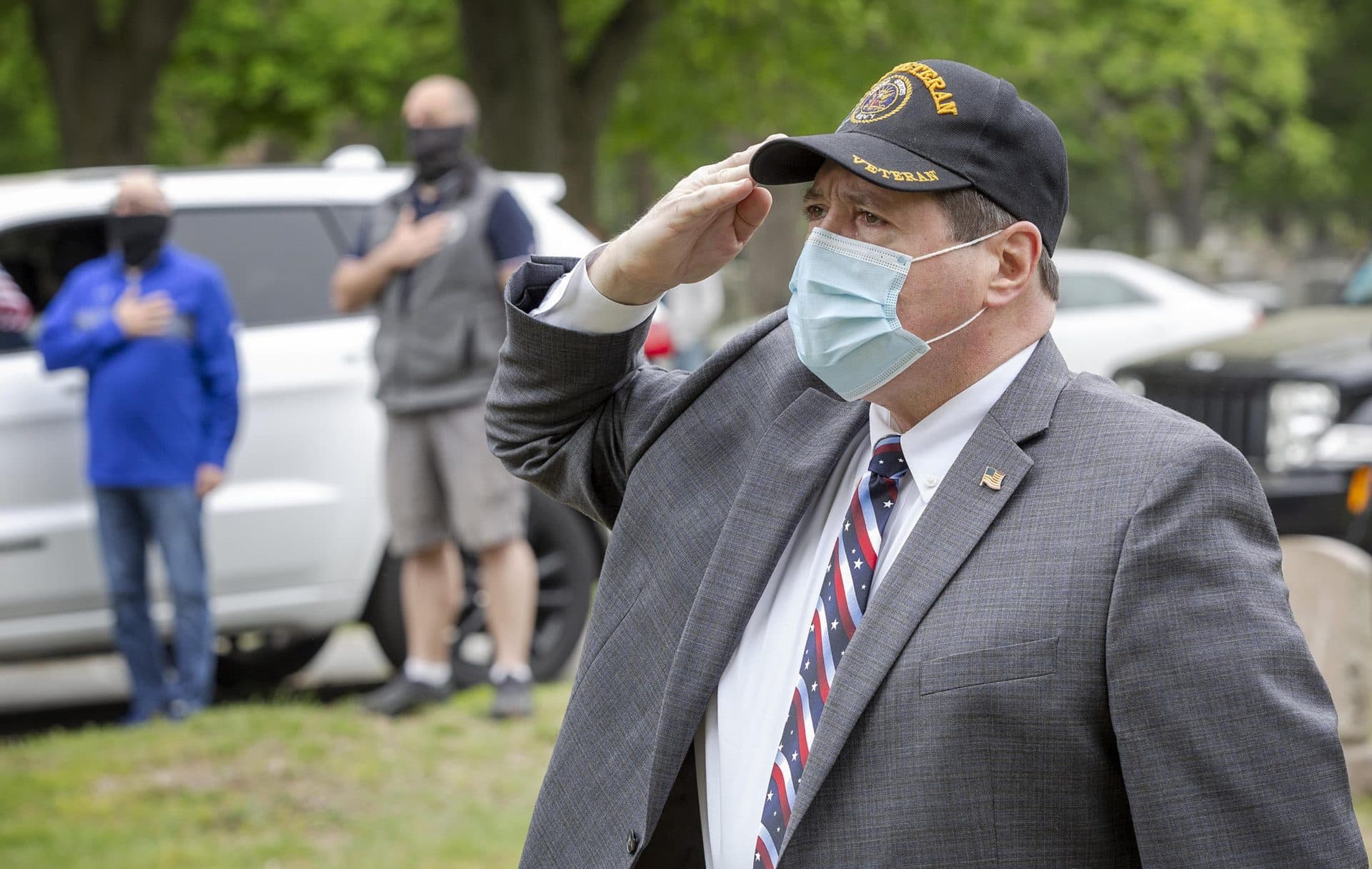 A man wearing a veteran hat salutes as the national anthem plays at a Memorial Day service in Glenwood Cemetery, Everett. (Robin Lubbock/WBUR)