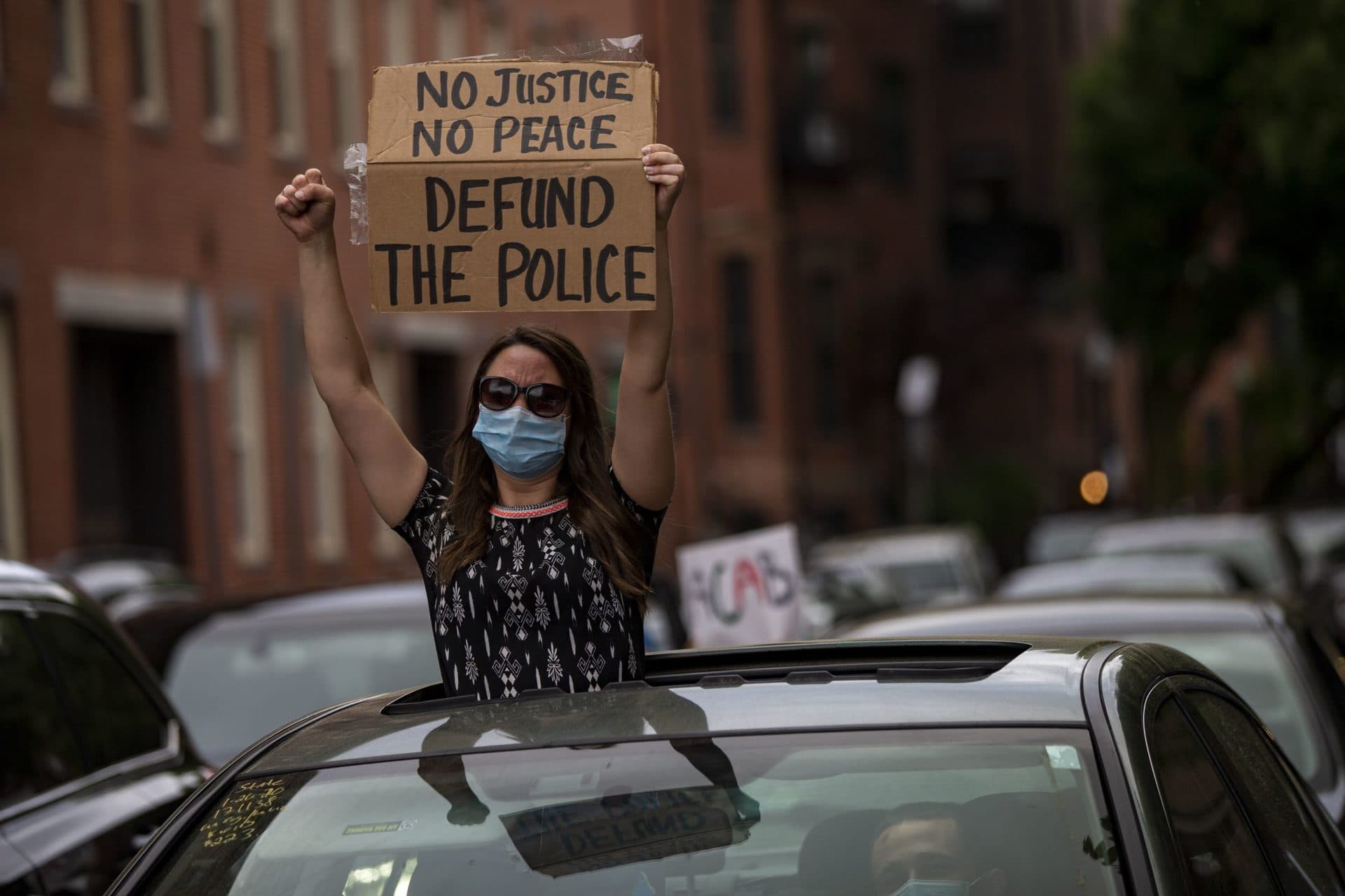 A protester holds a sign standing through the sunroof of a car while on Waltham Street. (Jesse Costa/WBUR)