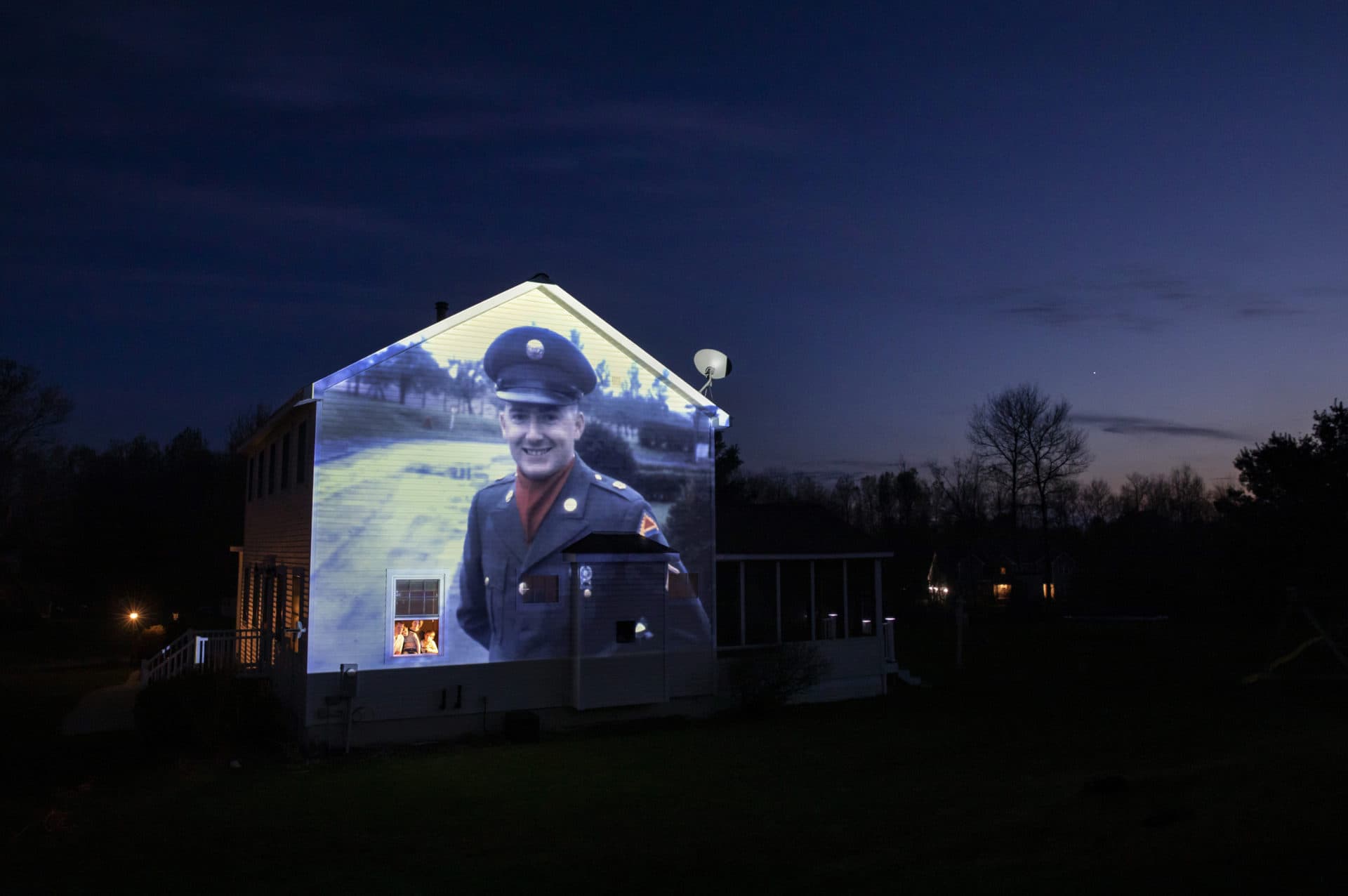 An image of veteran Chester LaPlante is projected onto the home of his son, Randy LaPlante, as he looks out a window with his wife, Nicole, and their sons, Evan and Blake, at their home in Amsterdam, N.Y. (David Goldman/AP)