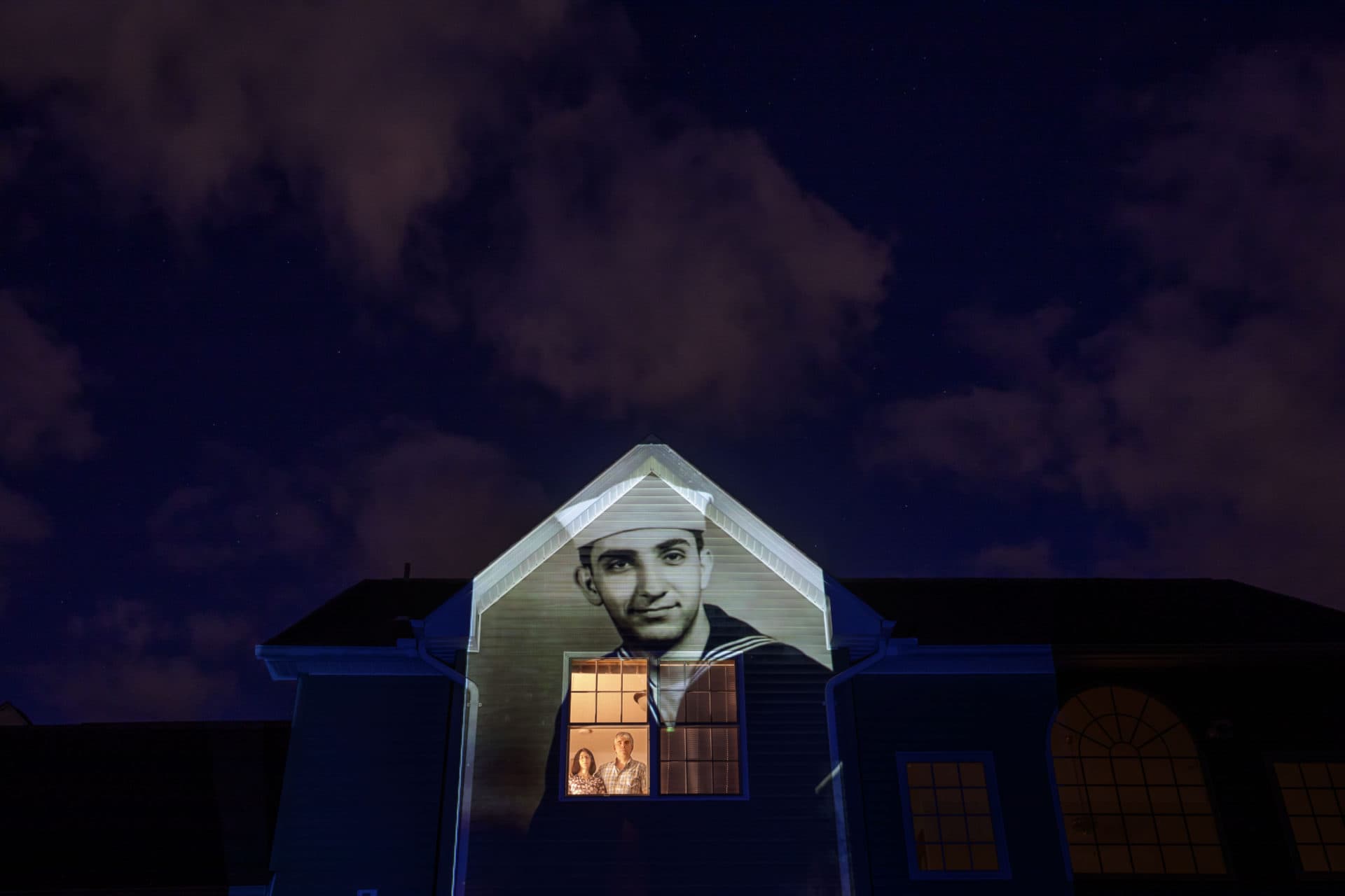 An image of veteran Harry Malandrinos is projected onto the home of his son, Paul Malandrinos, as he looks out a window with his wife, Cheryl, in Wilbraham, Mass. (David Goldman/AP)