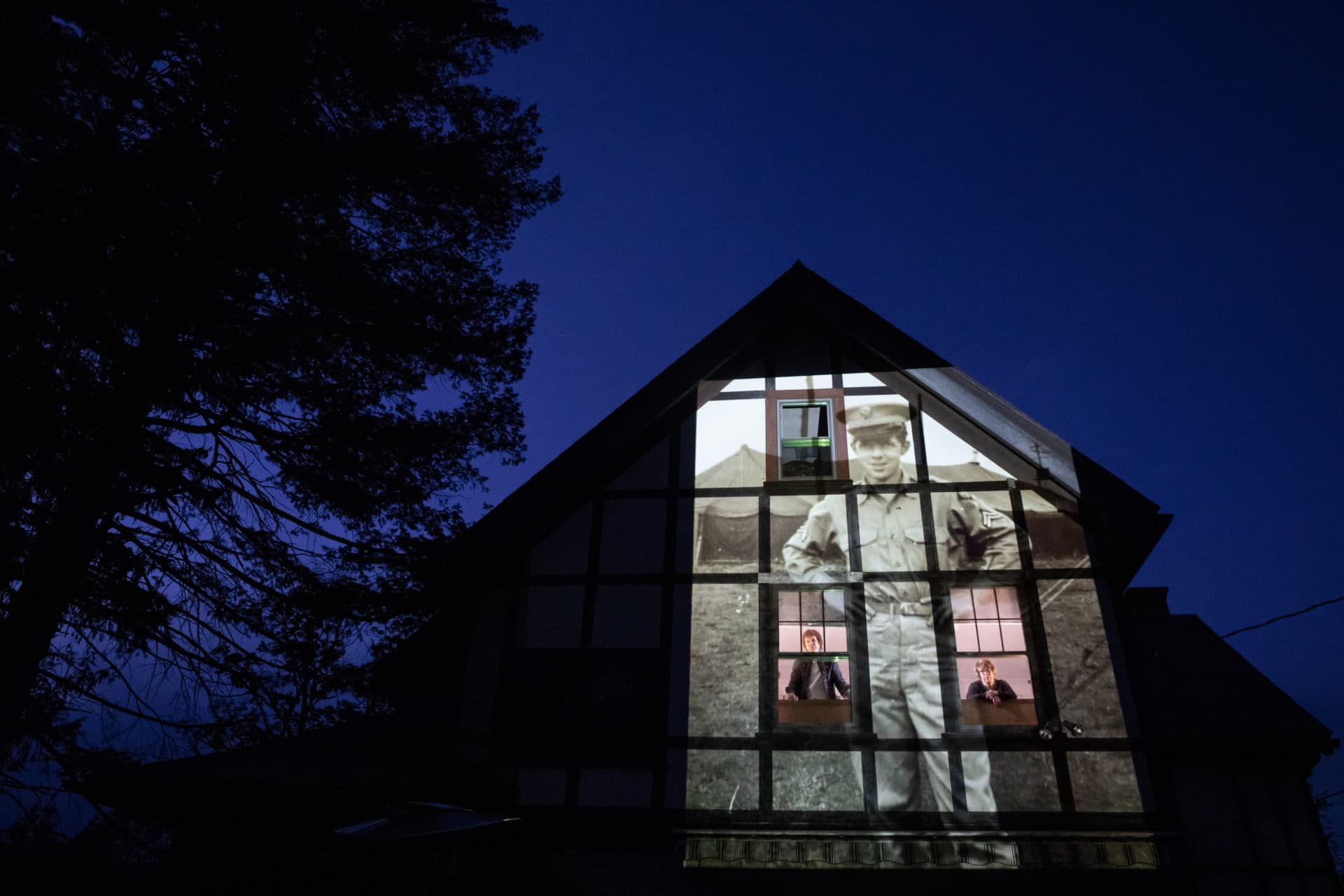 An image of veteran Alfred Healy is projected onto the home of his daughter, Eileen Driscoll, left, as she looks out the window with her sister, Patricia Creran, in Holyoke, Mass., (David Goldman/AP)