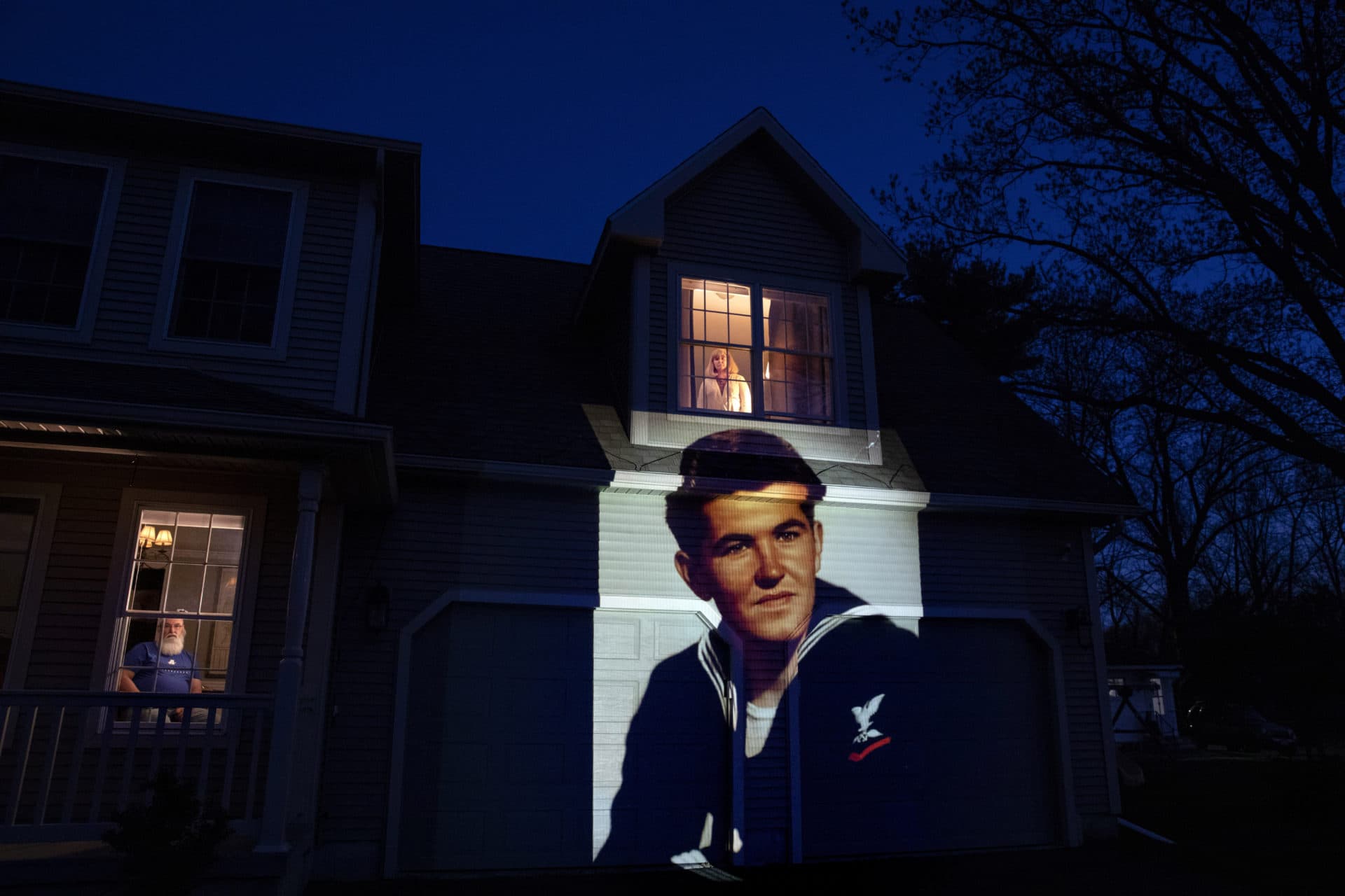 An image of veteran Stephen Kulig is projected onto the home of his daughter, Elizabeth DeForest, as she looks out the window of a spare bedroom as her husband, Kevin, sits downstairs in Chicopee, Mass. (David Goldman/AP)