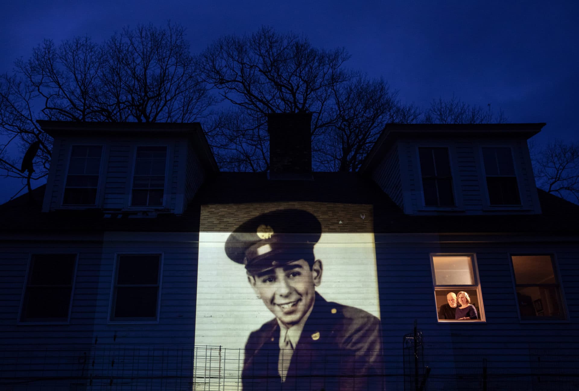 An image of veteran Emilio DiPalma, is projected onto the home of his daughter, Emily Aho, left, as she looks out a window with her husband, George, in Jaffrey, N.H. (David Goldman/AP)