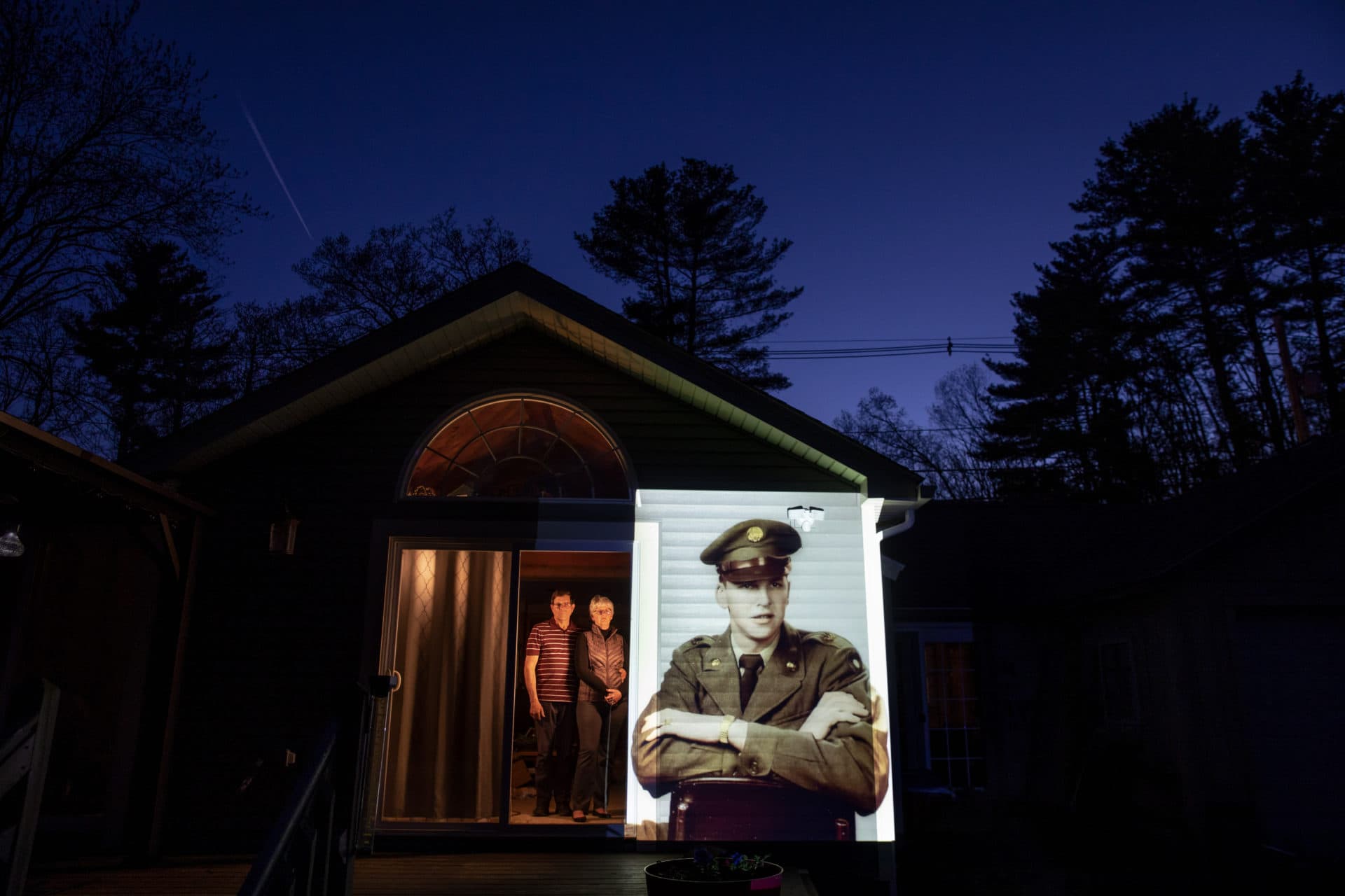 An image of veteran Roy Benson is projected onto the home of his daughter, Robin Benson Wilson, left, as she looks out a doorway with her husband, Donald, in Holland, Mass. (David Goldman/AP)