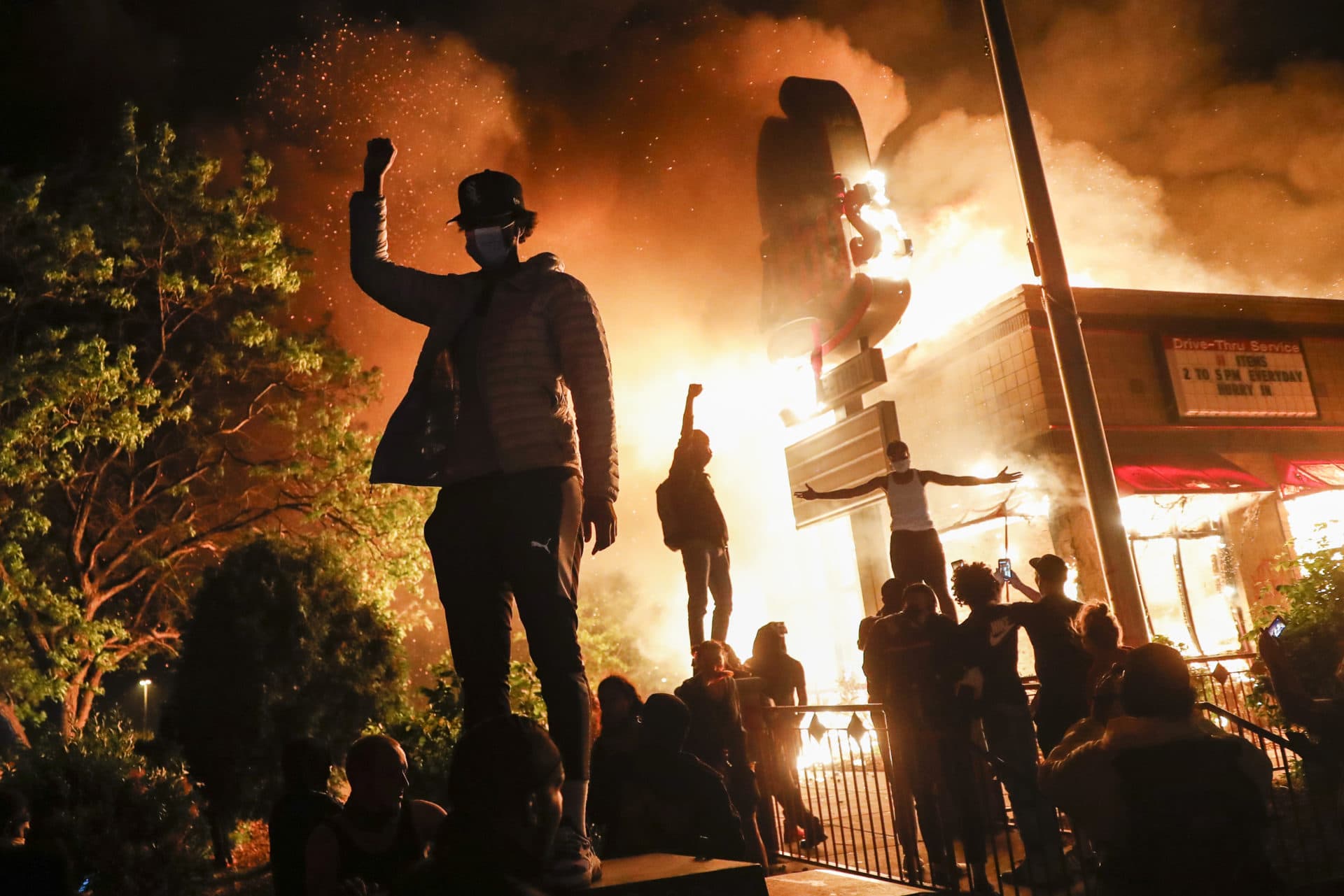 Protestors demonstrate outside of a burning fast food restaurant, Friday, May 29, 2020, in Minneapolis. (AP Photo/John Minchillo)