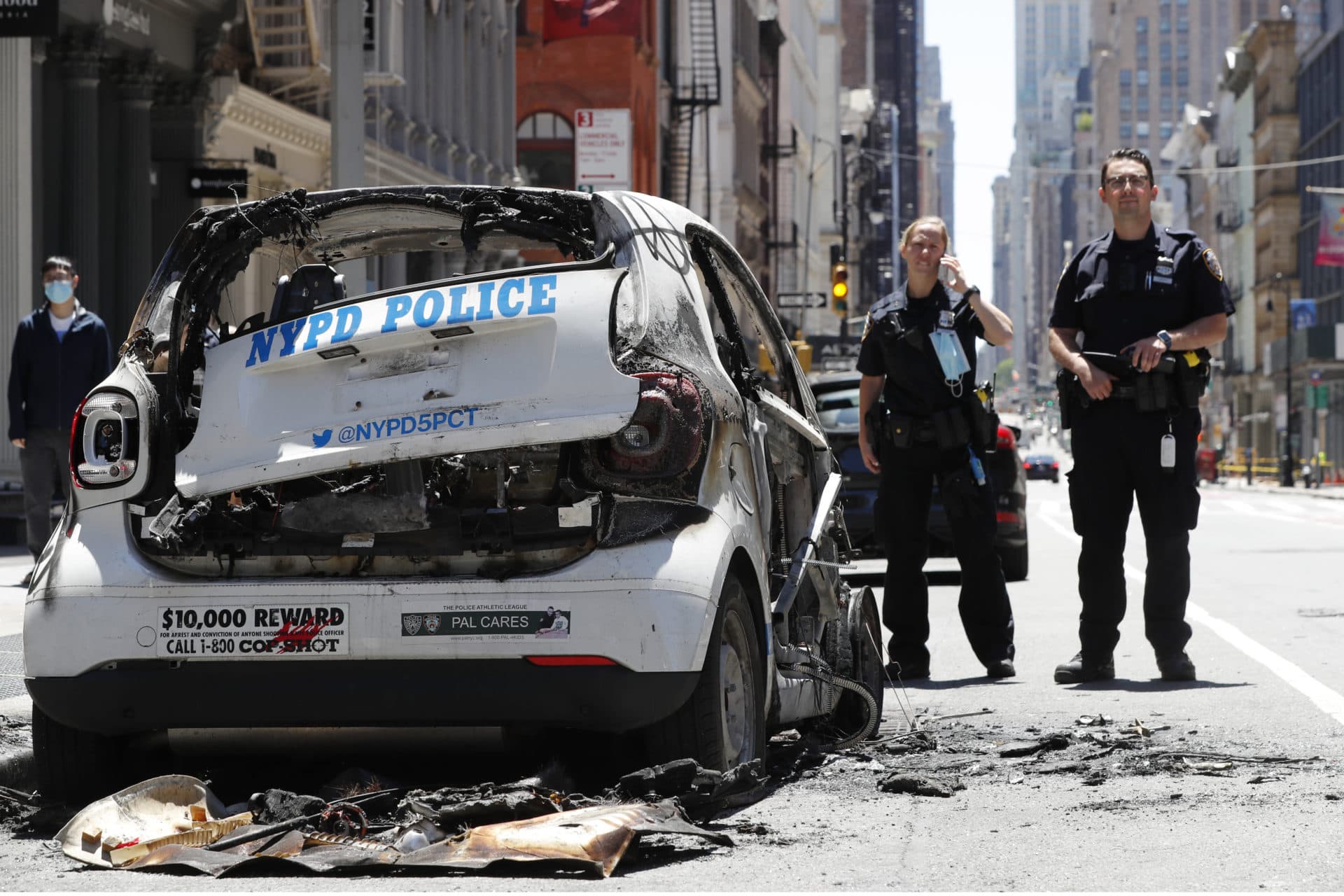 Officers stand guard beside a burned-out mini-New York Police Department vehicle, abandoned on Broadway in Lower Manhattan, Sunday, May 31, 2020, in New York. (AP Photo/Kathy Willens)
