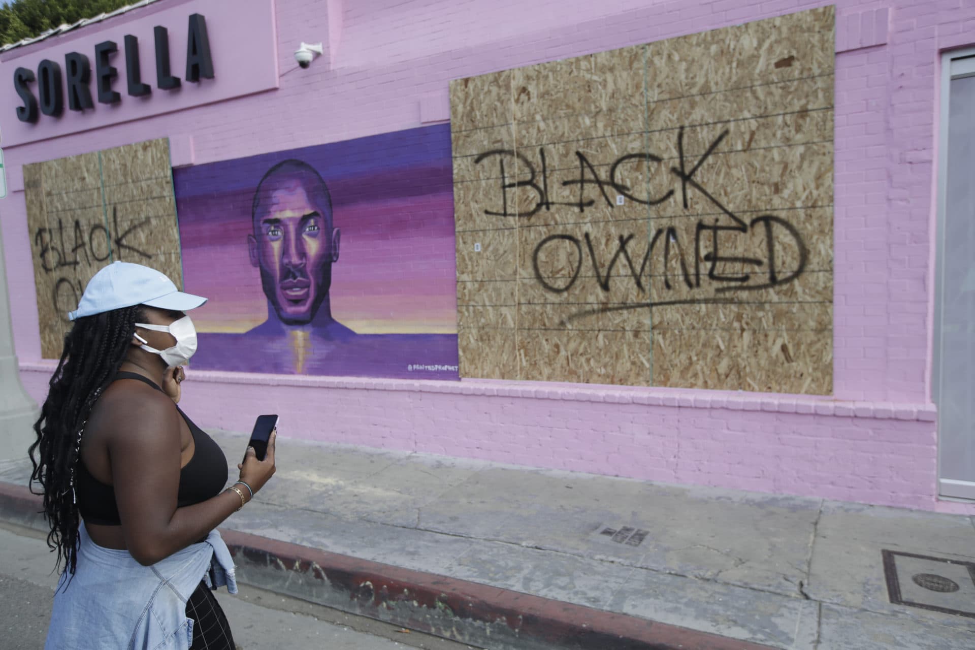 A woman looks at a boarded up store front, Sunday, May 31, 2020, in Los Angeles, following a night of unrest and protests over the death of George Floyd, a black man who was in police custody in Minneapolis. Floyd died after being restrained by Minneapolis police officers on May 25. (AP Photo/Marcio Jose Sanchez)