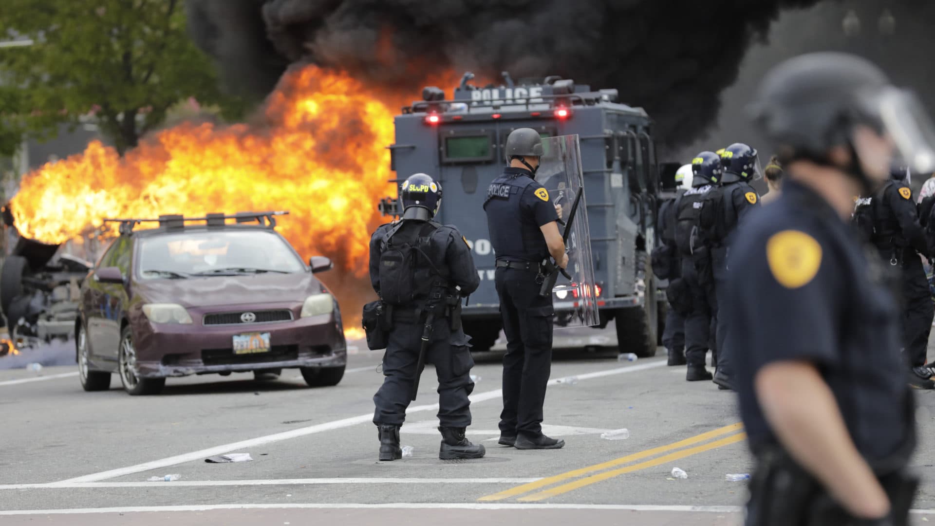 Policemen watch as a vehicle burns as protesters demonstrate Saturday, May 30, 2020, in Salt Lake City. Thousands of people converged on downtown Salt Lake City on Saturday to protest the death of George Floyd in Minneapolis, and some demonstrators set fire to a police car and threw eggs and wrote graffiti on a police station. (AP Photo/Rick Bowmer)