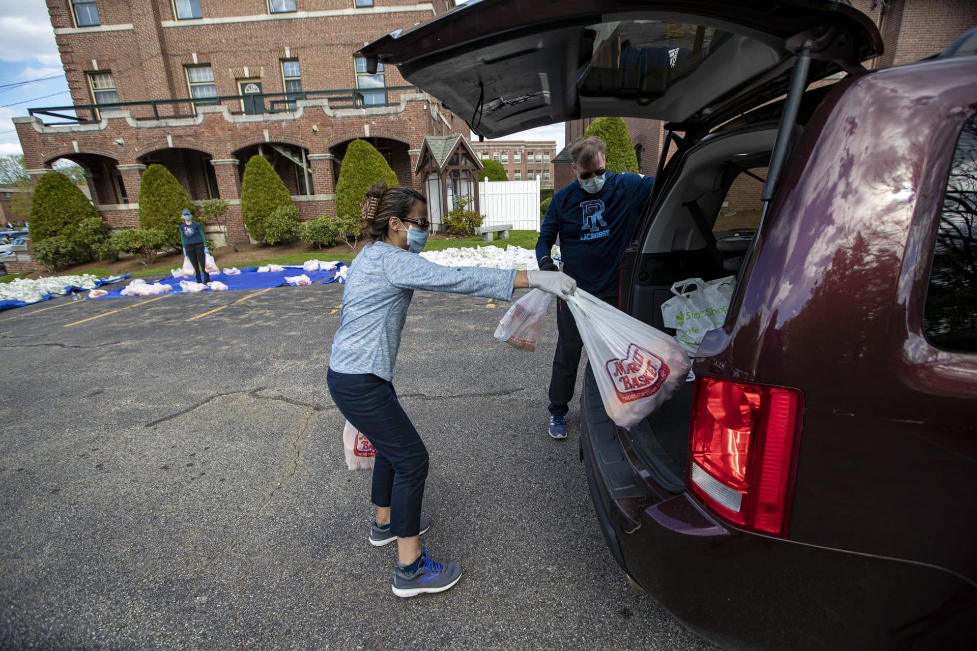 A volunteer places bags of groceries into the back of a minivan. (Jesse Costa/WBUR)
