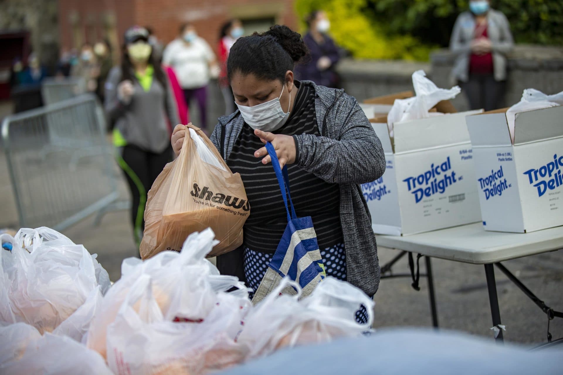 A woman picks up a prepared bag of food supplies. Hundreds of people and families lined up on foot and in their vehicles at St. Mary Parish in Waltham on a recent Thursday to receive food assistance. (Jesse Costa/WBUR)