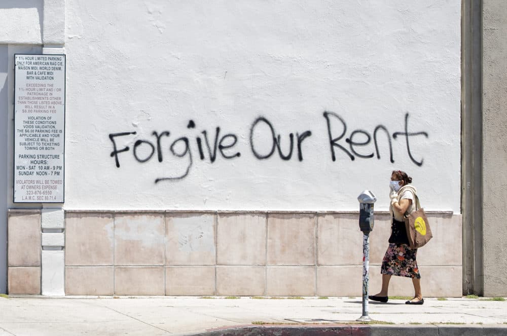 A woman wearing a mask walks past a wall bearing a graffiti asking for rent forgiveness on La Brea Ave on National May Day amid the Covid-19 pandemic, May 1, 2020, in Los Angeles, California. (VALERIE MACON/AFP via Getty Images)