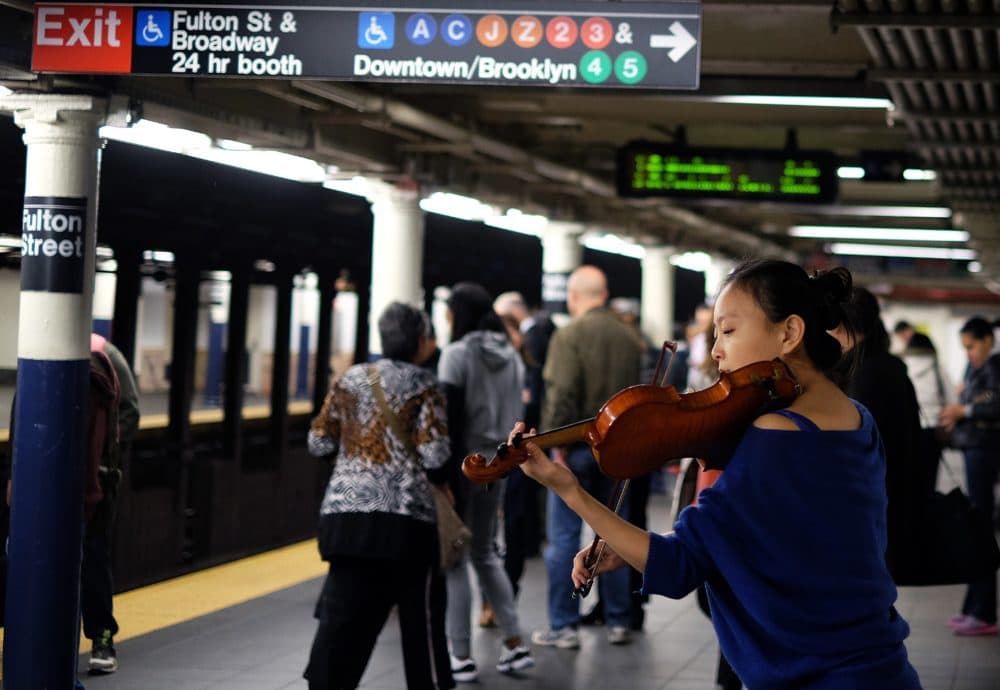 A musician plays violin as commuters wait to catch their train at the Fulton Center subway station in New York on November 10, 2014. (Jewel Samad/AFP via Getty Images)
