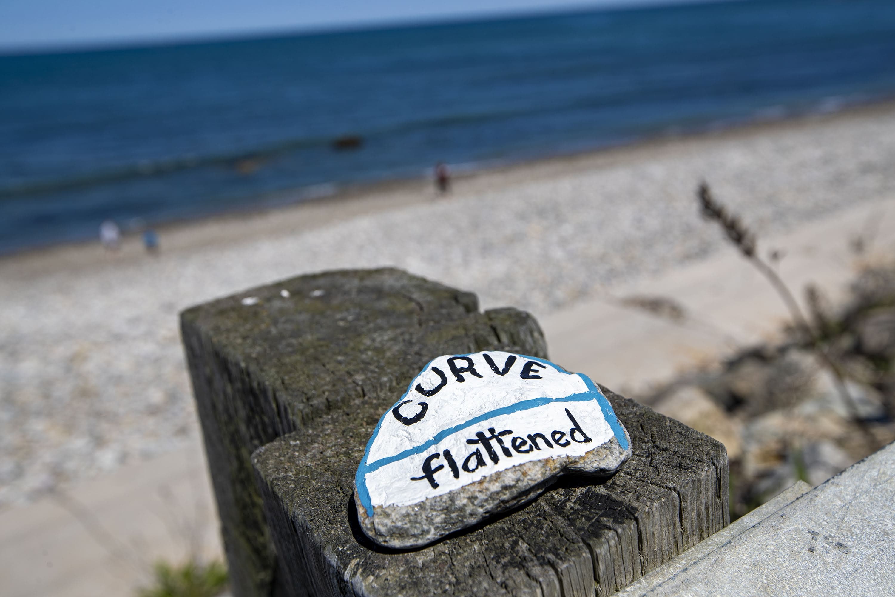 Brightly painted rocks with messages inscribed on them in response to the pandemic are left on top of the guardrails at a virtually empty Brant Rock Beach in Marshfield. (Jesse Costa/WBUR)