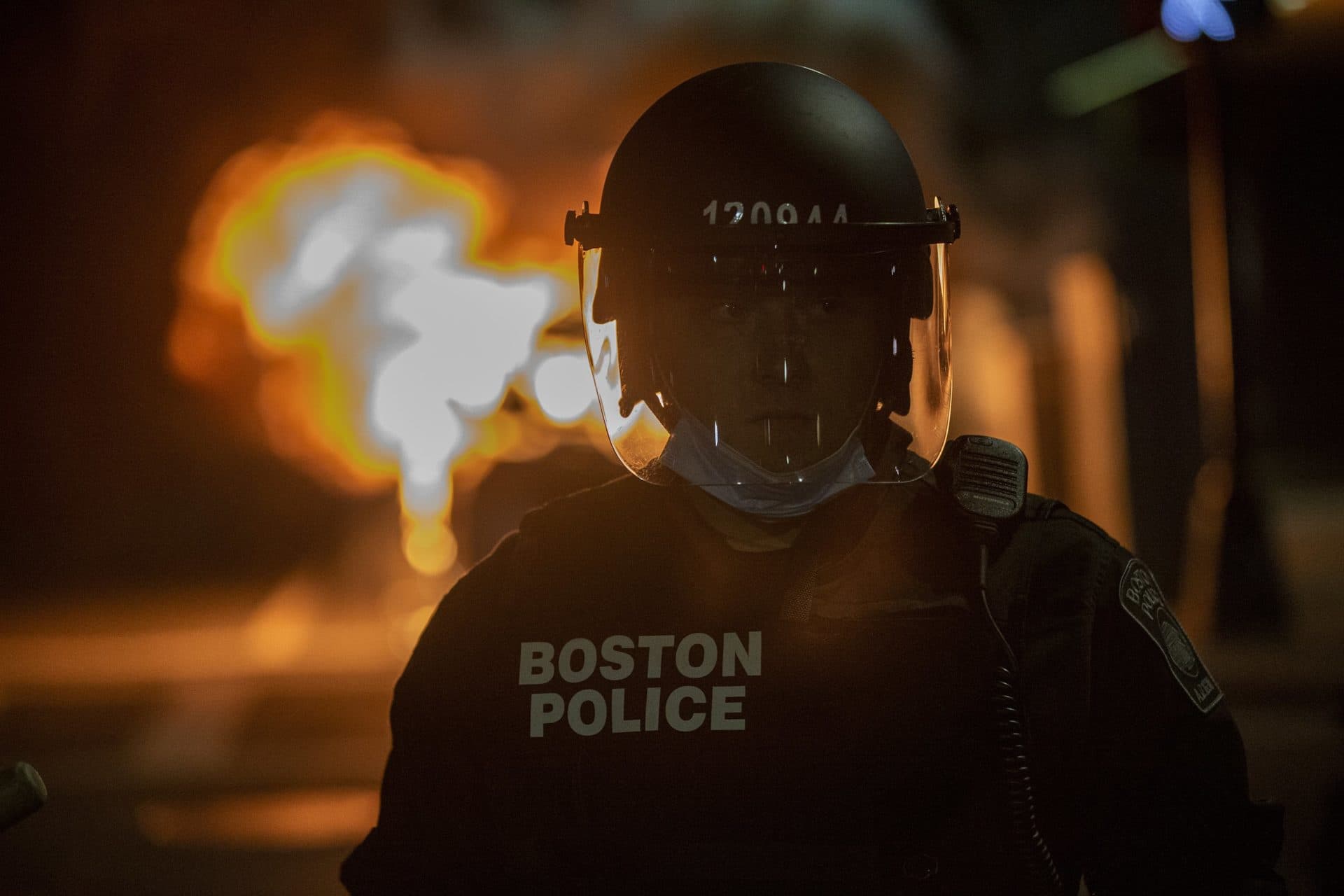 A Boston Police officer looks around as a Police SUV is on fire behind him on Tremont Street. (Jesse Costa/WBUR)