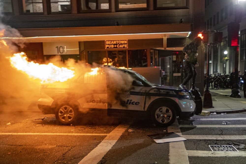 A protester walks on a Boston Police cruiser set fire on Tremont Street after a March 31 protest near the Massachusetts
State House. (Jesse Costa/WBUR)