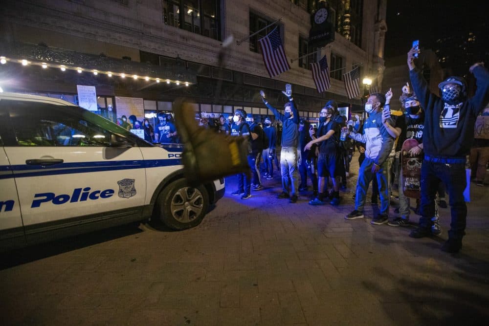 A boot is thrown at a Boston Police vehicle as protesters stand in front of a cruiser Downtown Crossing. (Jesse Costa/WBUR)