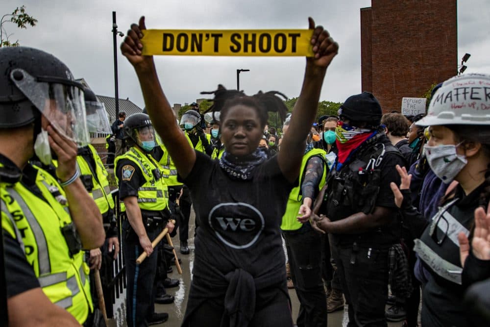 A protester holds up caution tape that read “Don’t Shoot” as police and protester stand off in front of Forest Hills station in Jamaica Plain. (Jesse Costa/WBUR)