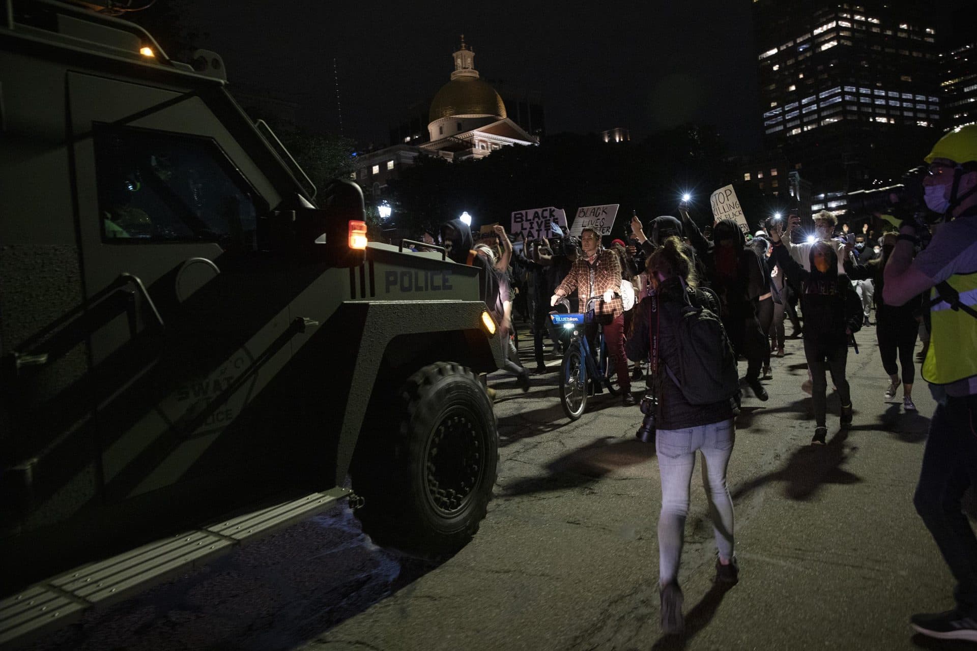 An armored police vehicle reverses down Beacon Street followed by a group of protesters. (Robin Lubbock/WBUR)