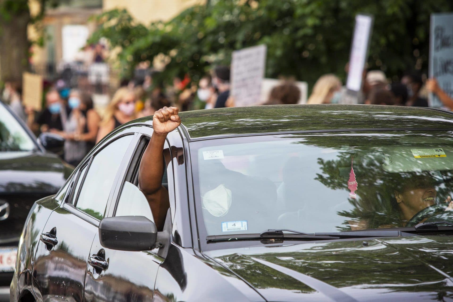 With cars honking their horns, a man holds a clenched fist up out of his car window as he passes Adams Park. (Robin Lubbock/WBUR)