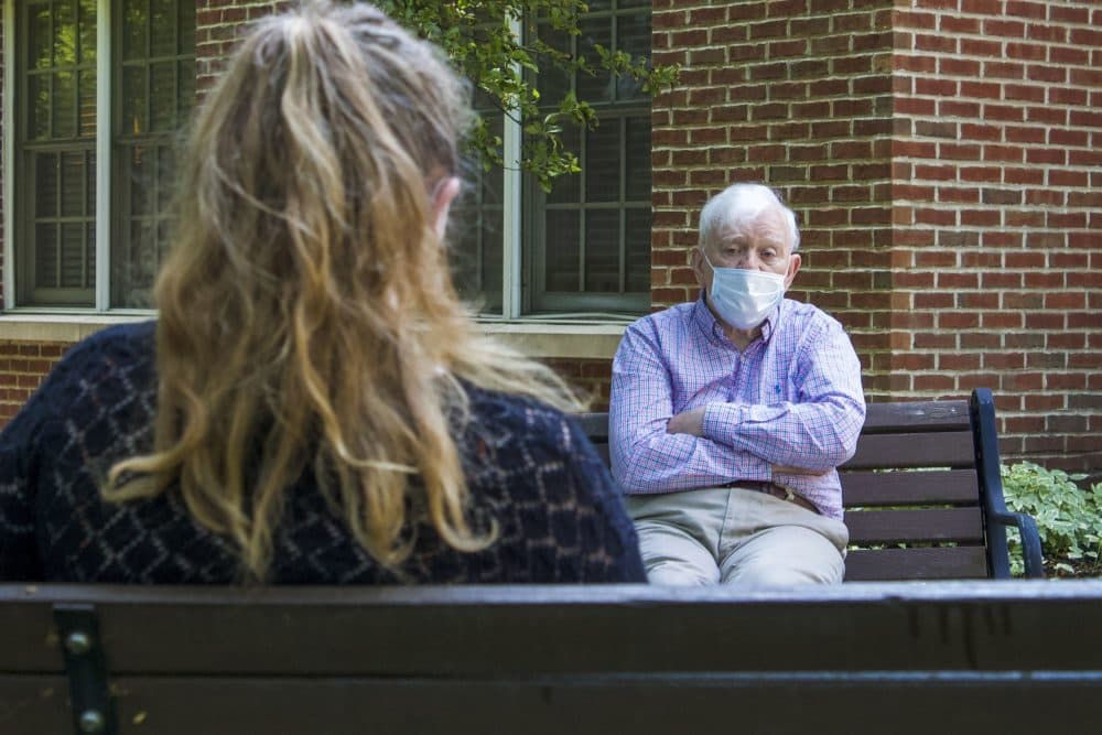 Claire and Geoffrey Davies sit six feet apart and wear masks during their visit at Rogerson House in Boston.(Miriam Wasser/WBUR)