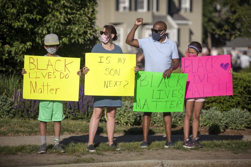 Protesters stand on the Centre Street traffic circle in West Roxbury waving at cars, during Monday’s Vigil For Black Lives. (Robin Lubbock/WBUR)