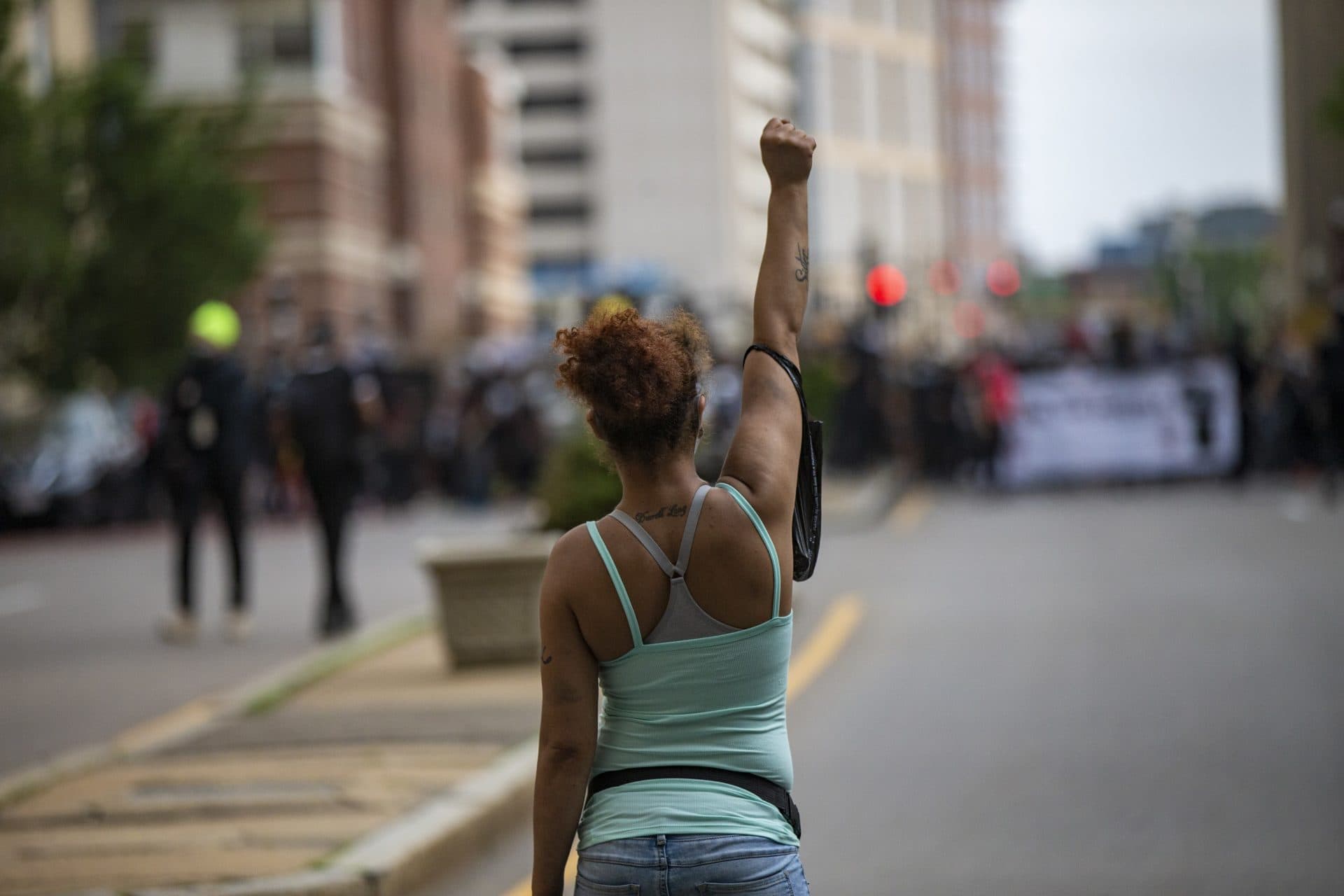A woman raises her fist in the middle of the street by Tufts Medical Center as hundrreds of protesters march up Washington Street en route to Boston City Hall during the F.T.P. March to Defund Police and Fund Our Communities. (Jesse Costa/WBUR)