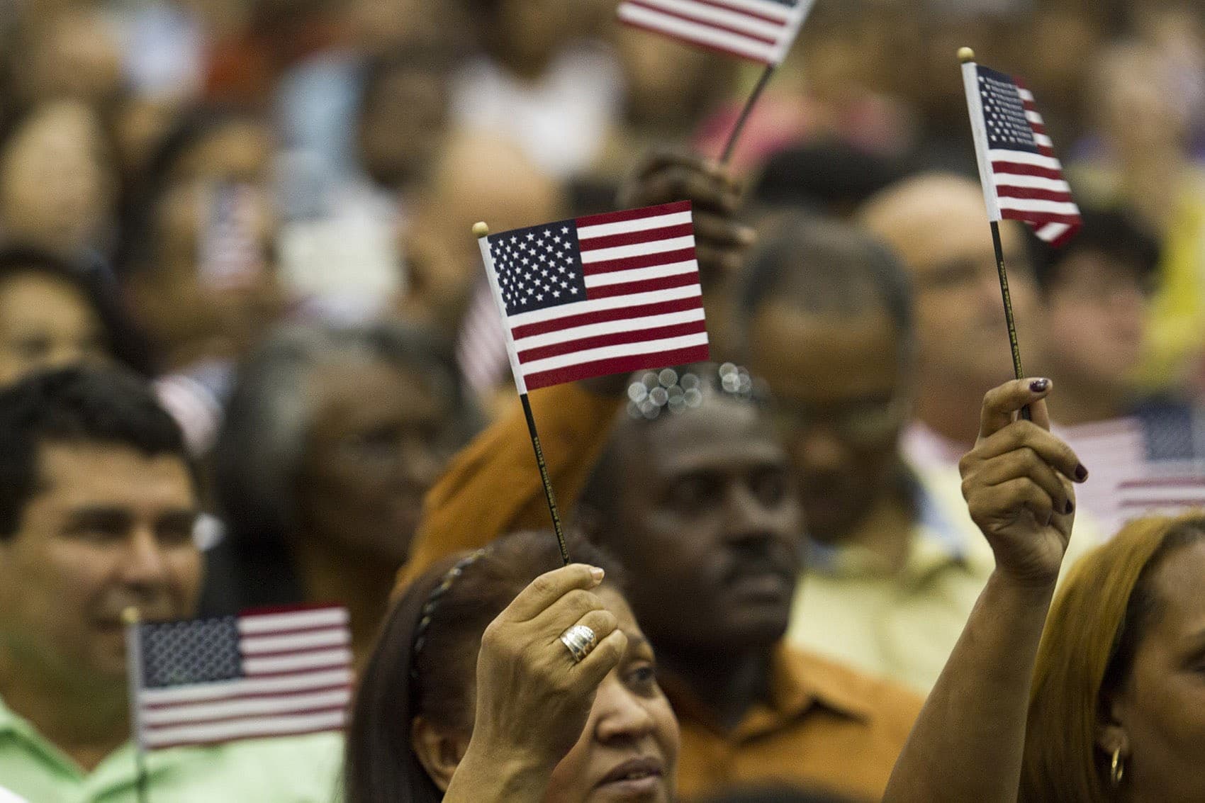 Brand-new U.S. citizens wave flags during a rendition of “America the Beautiful” at the Hynes Convention Center in 2016. (Joe Difazio for WBUR)