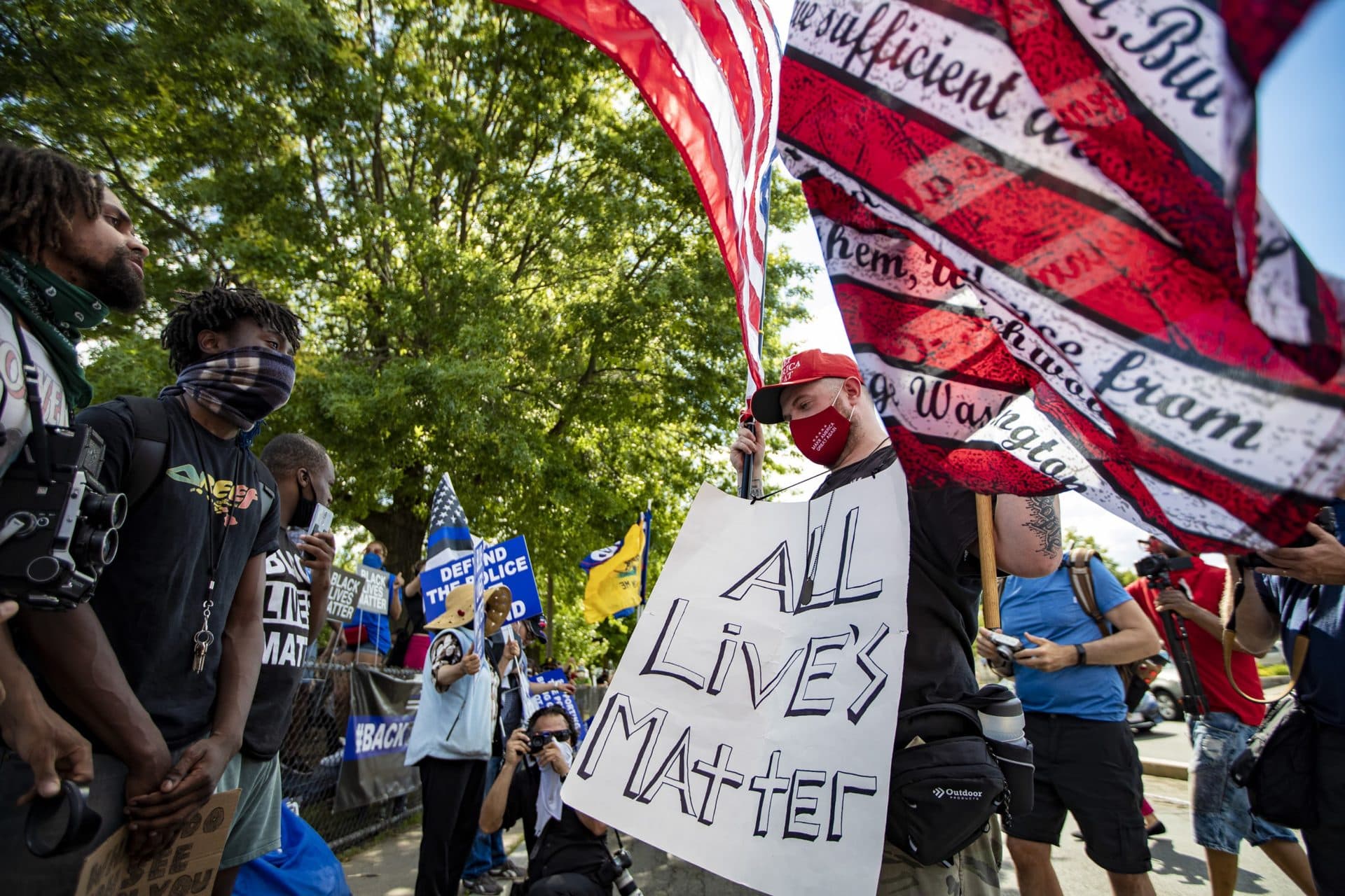 A Blue Lives Matter supporter holds up two American flags while Black Lives Matter rally participants speak to him during a rally at Town Field in Dorcester. (Jesse Costa/WBUR)