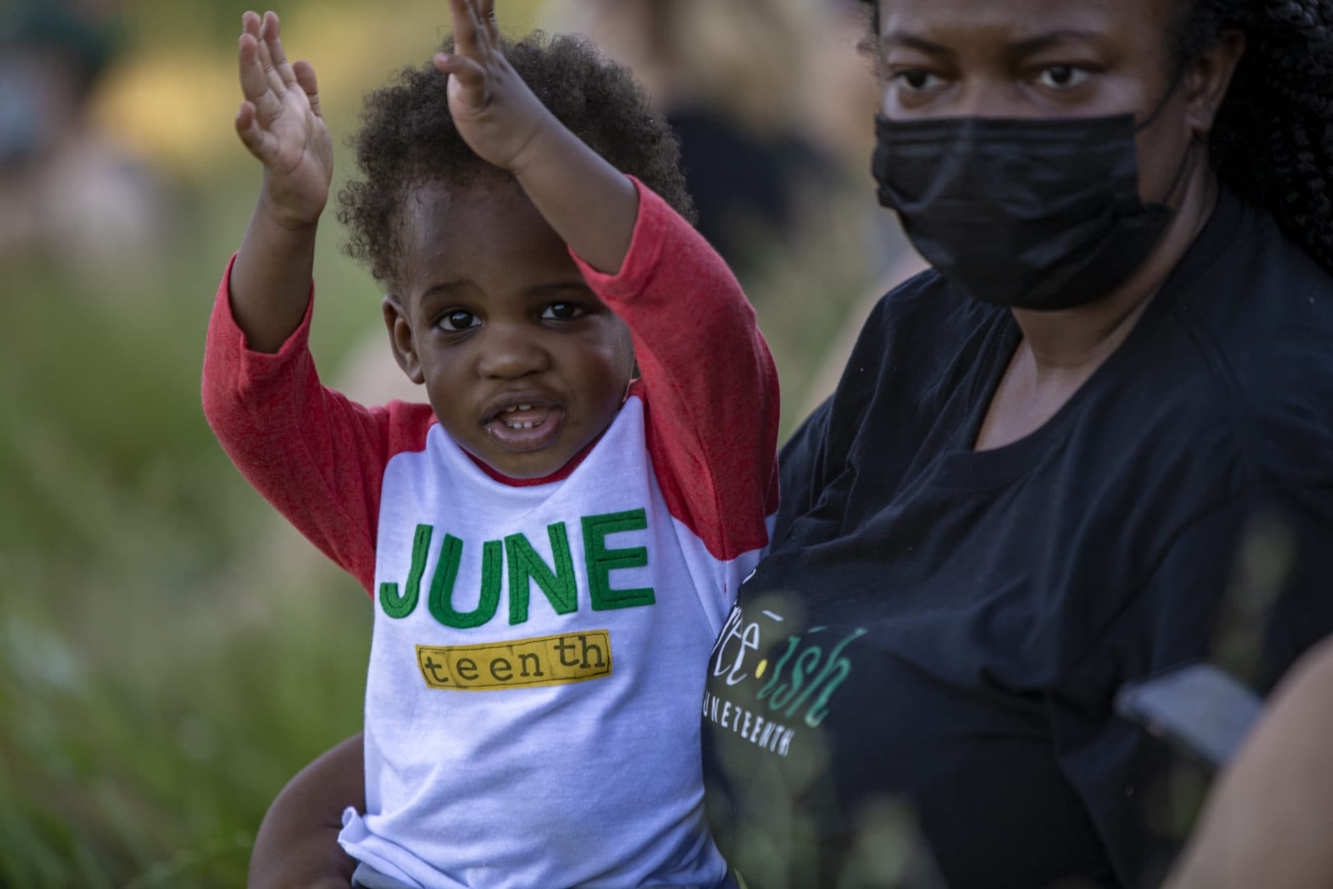 A young boy wearing a Juneteeth shirt applauds with the rest of the crowd during the "Funk the Police" rally at Ronan Park in Dorchester. (Jesse Costa/WBUR)