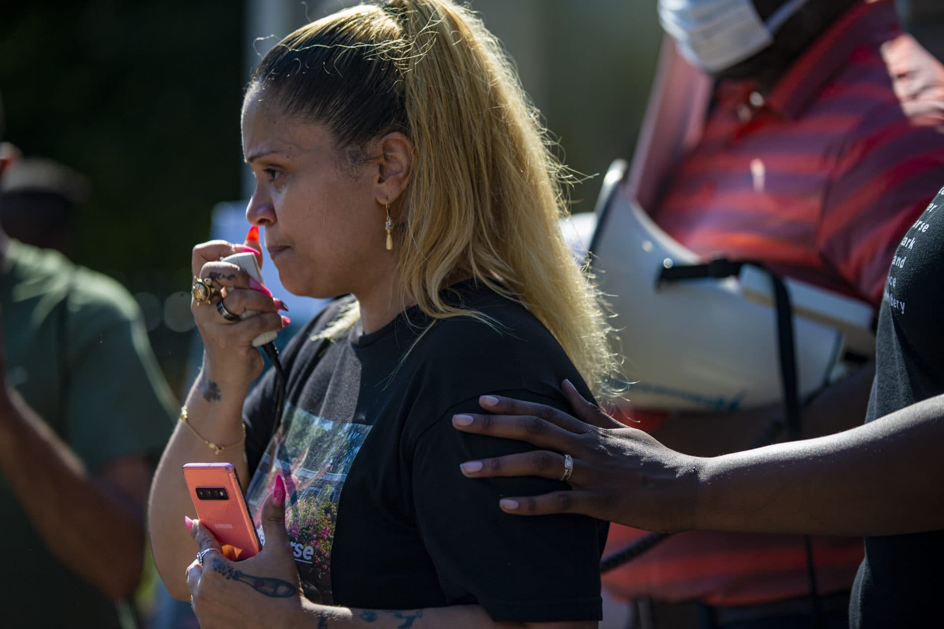 Monica Cannon-Grant touches the shoulder of Angelique Negroni-Kearse, as she pauses during a speech in front of the State House. Negroni-Kearse is the widow of Andrew Kearse who died in police custody after being denied medical care in 2017 in Schenectady, New York. (Jesse Costa/WBUR)
