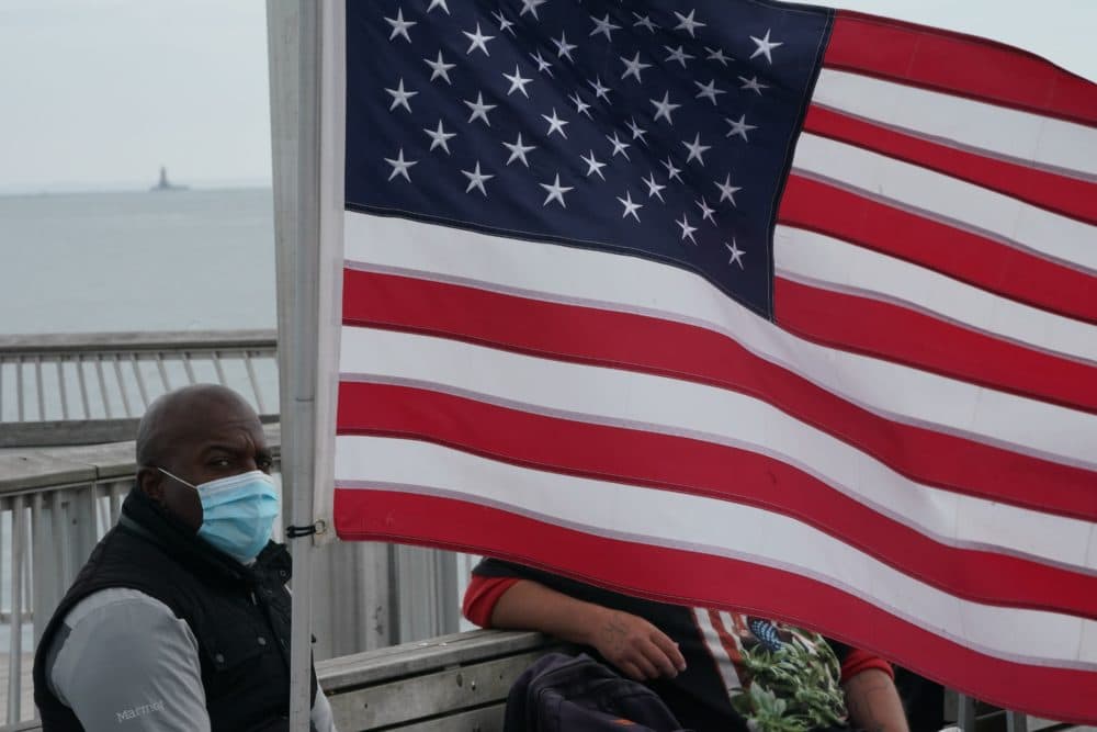 A man wearing a face mask sits near an American flag on a pier at Coney Island amid the coronavirus pandemic on May 24, 2020 in New York. (Bryan R. Smith/AFP/Getty Images)