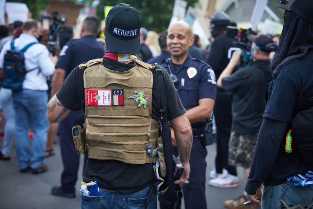 A member of the far-right militia, Boogaloo Bois, walks next to protesters demonstrating outside Charlotte Mecklenburg Police Department Metro Division 2 just outside of downtown Charlotte, North Carolina, on May 29, 2020. (Logan Cyrus/AFP/Getty Images)