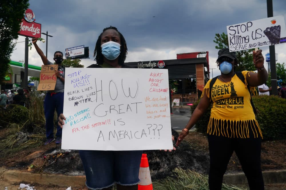 People hold signs toward traffic outside a burned Wendys restaurant on the second day following the police shooting death of Rayshard Brooks in the restaurant parking lot June 14, 2020, in Atlanta, Georgia. (ELIJAH NOUVELAGE/AFP via Getty Images)