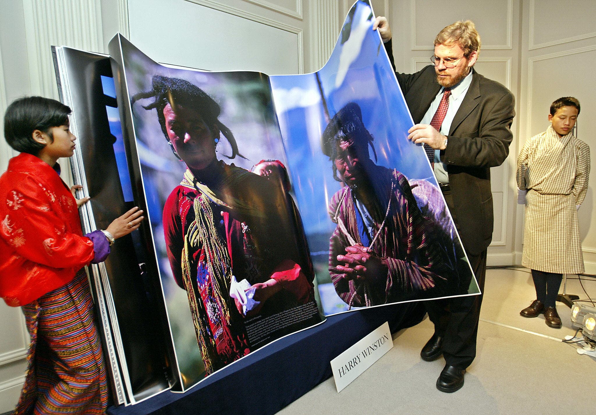 In this 2003 photo, MIT's Michael Hawley turns a page of his book "Bhutan, A Visual Odyssey Across the Kingdom" to introduce the Himalayan country while Bhutanese boy Gyelsey Loday (R) and girl Choki Lhamo (L) look on during a preview in Tokyo. (TORU YAMANAKA/AFP via Getty Images)