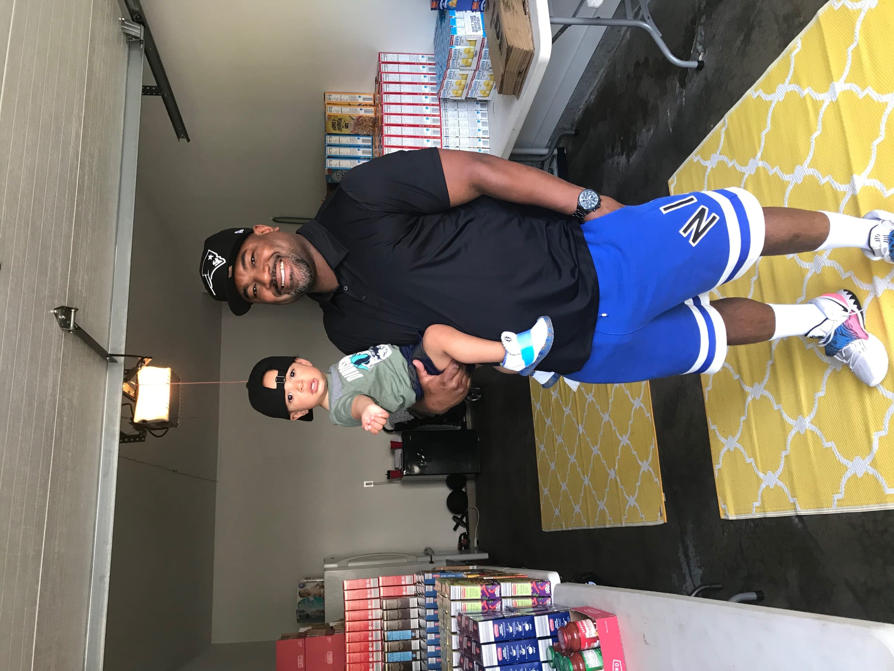 Maurice Humphrey and his son, MJ, pose in their garage, where Maurice keeps the stockpile of groceries he distributes to families in need in Connecticut -- all purchased from donated funds collected through his "$20 Challenge." (Courtesy)