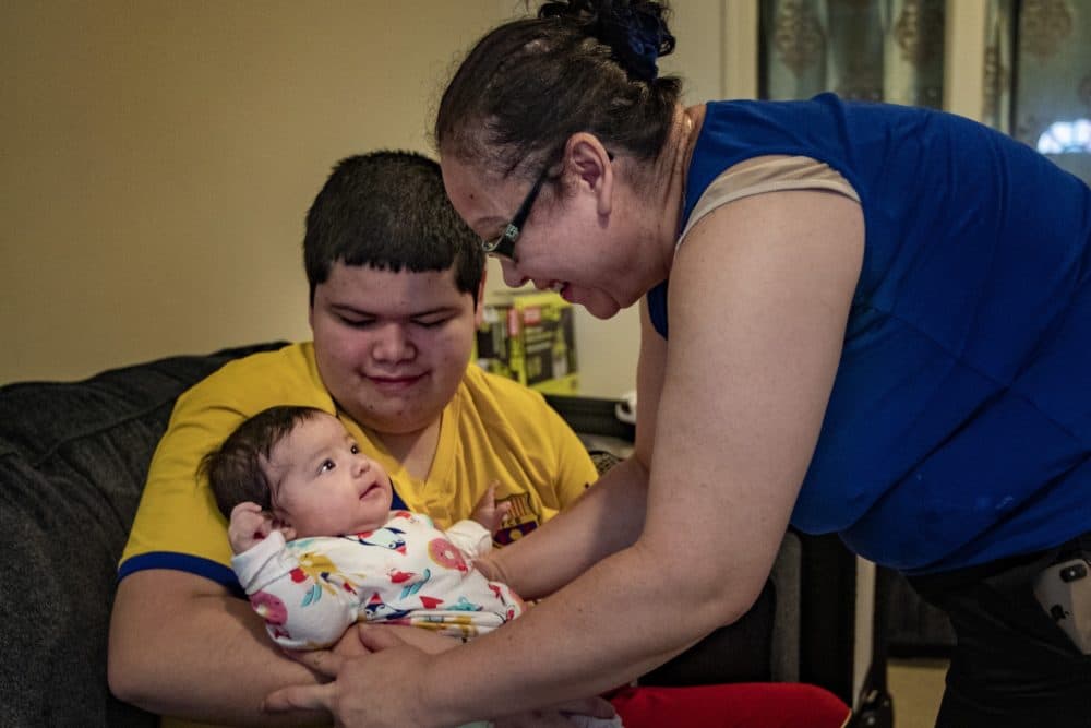 Carolina takes her 4-month-old daughter from her son. (Jesse Costa/WBUR)