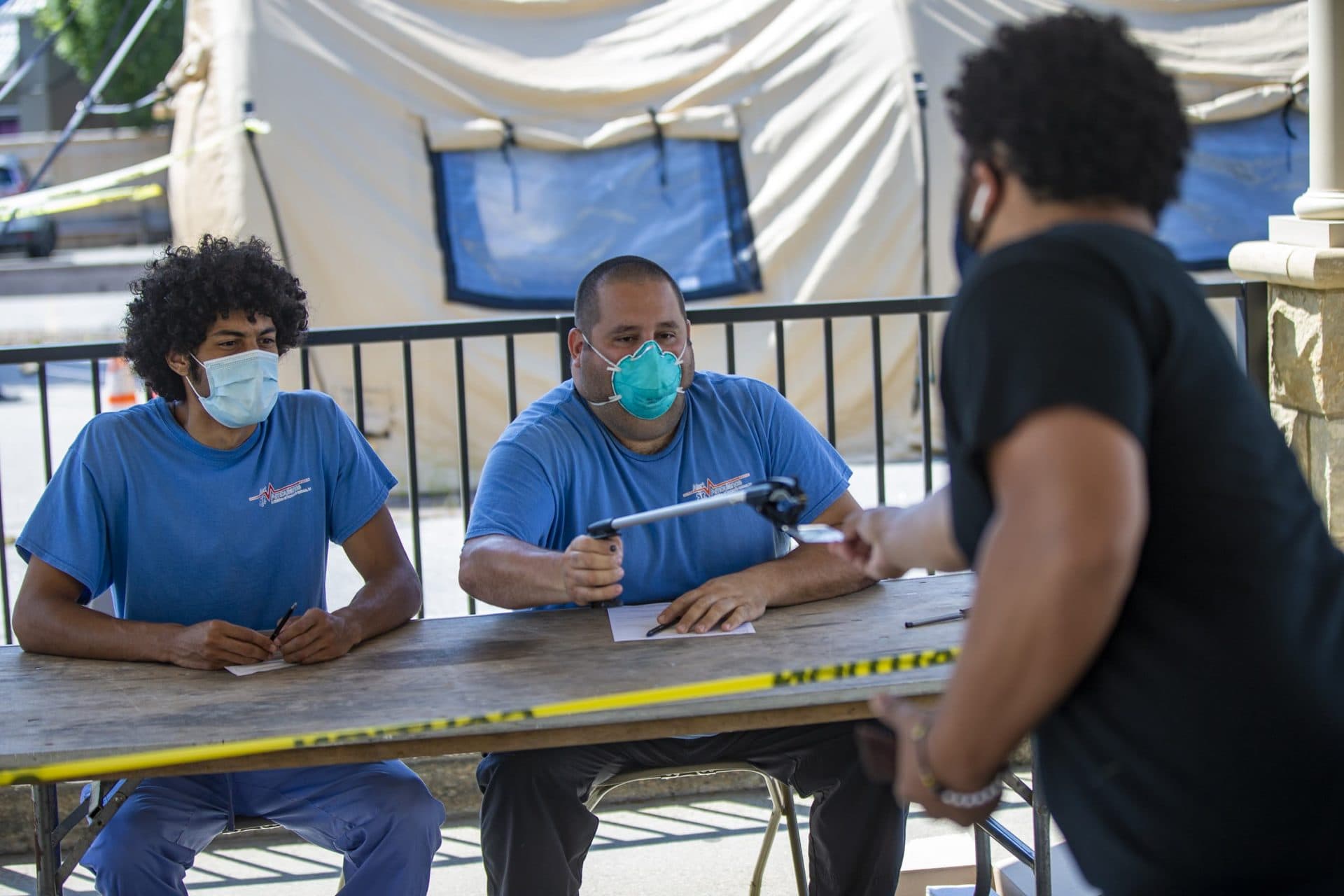 Health workers at the Rhode Island College walk-up testing site in Central Falls use a reacher tool to take the identification from a man requesting to be tested for COVID-19. (Jesse Costa/WBUR)