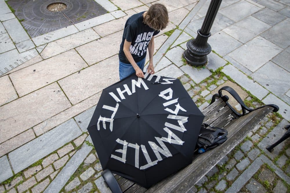 A protester applies white tape on an umbrella spelling out the words “Dismantle White Supremecy” before the march. (Jesse Costa/WBUR)