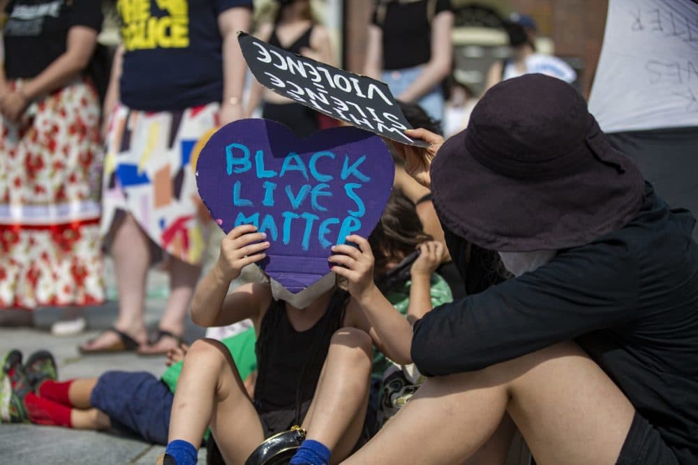 A young girl uses a Black Lives Matter sign to block the sun. (Jesse Costa/WBUR)