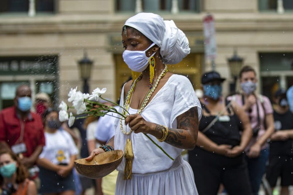 A member of the Sistahs of the Calabash sprays water around the site of the Boston Massacre, a ritual to begin the celebration of song and dance during the march. (Jesse Costa/WBUR)