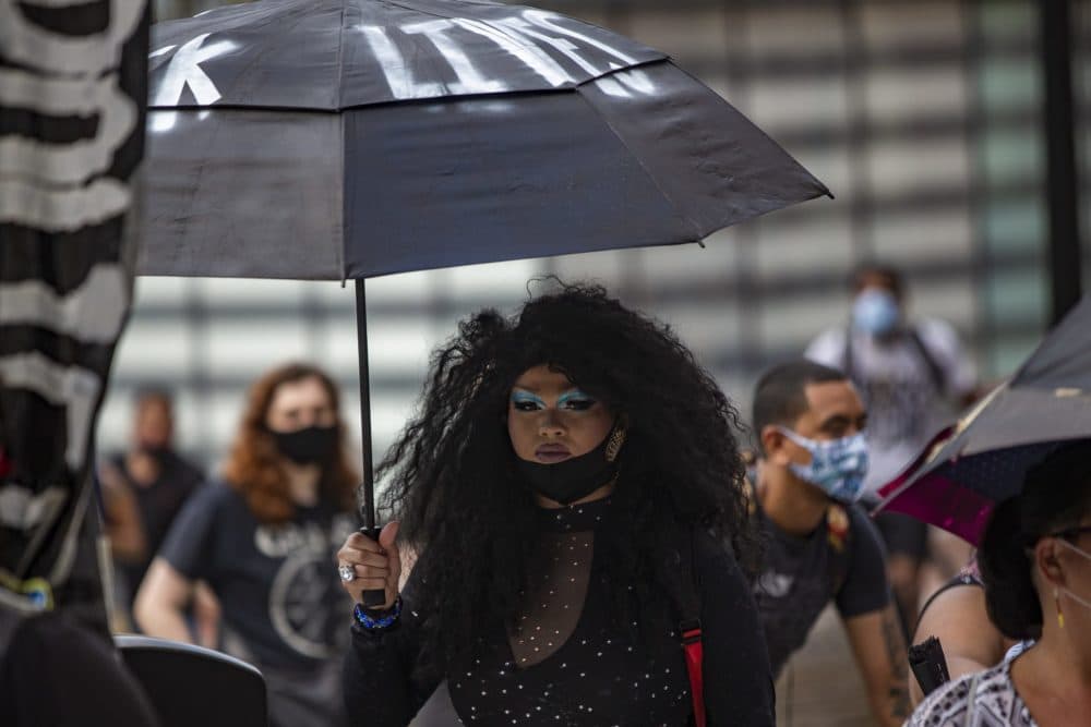 A protester stands with an umbrella while listening to speeches in front of Faneuil Hall. (Jesse Costa/WBUR)
