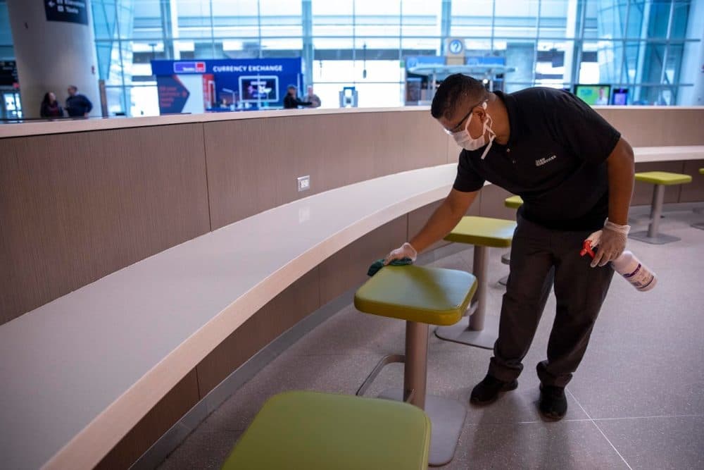 Juan Nunez disinfects seats in the arrivals area of Terminal E at Logan Airport in March. (Robin Lubbock/WBUR)