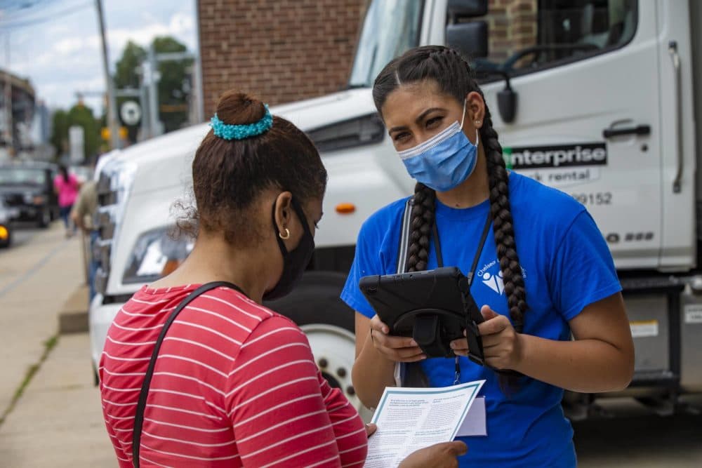 With a tablet, Chelsea Collaborative volunteer Yudalys Escobar assists a Chelsea resident fill out the 2020 census during a food distribution event on 6th Street. (Jesse Costa/WBUR)