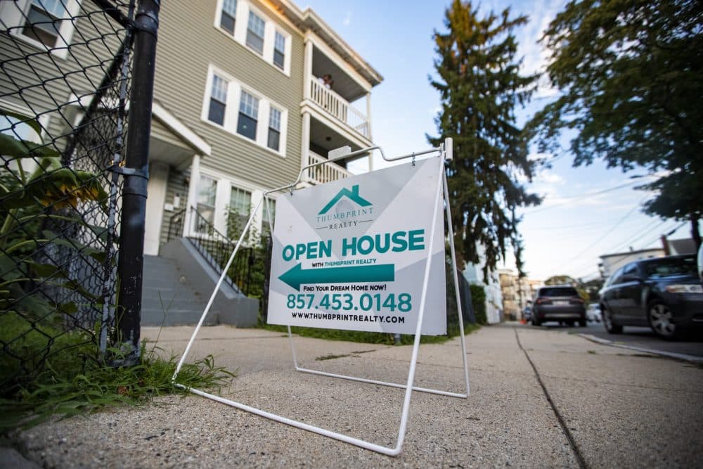 An open house sign outside of Mindy Wright’s condominium in Dorchester, as realtor Jonathan Viciere stands on the third floor porch looking for any interested parties. (Jesse Costa/WBUR)