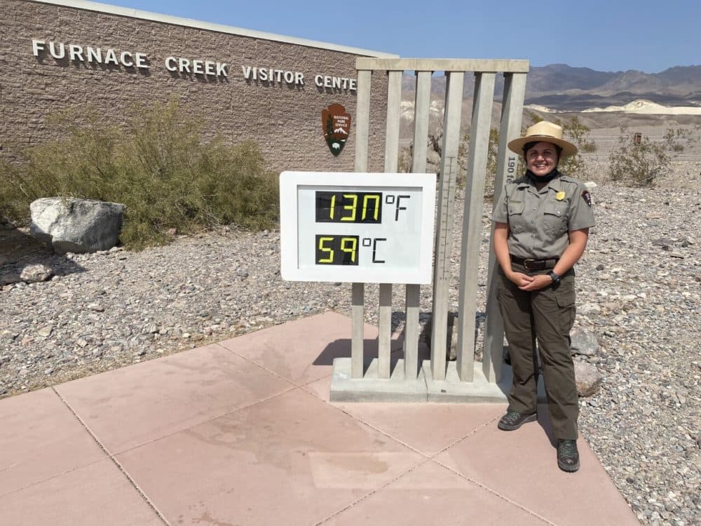 Brandi Stewart, education and program outreach manager at Death Valley National Park, stands near a thermometer that reads 130 degrees.
