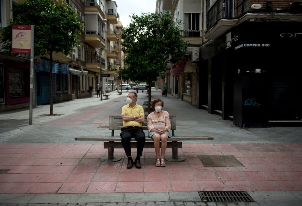 An elderly couple wearing face masks sits on a bench in Seville on May 7, 2020. (CRISTINA QUICLER/AFP via Getty Images)