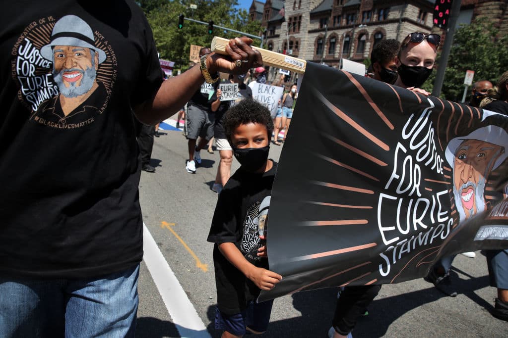 A family holds a flag during a march calling justice for Eurie Stamps that began at City Hall in Cambridge on Aug. 1, 2020. Eurie Stamps was a 68-year-old man who was accidentally shot and killed by police during a 2011 drug raid at his home. (Craig F. Walker/The Boston Globe via Getty Images)