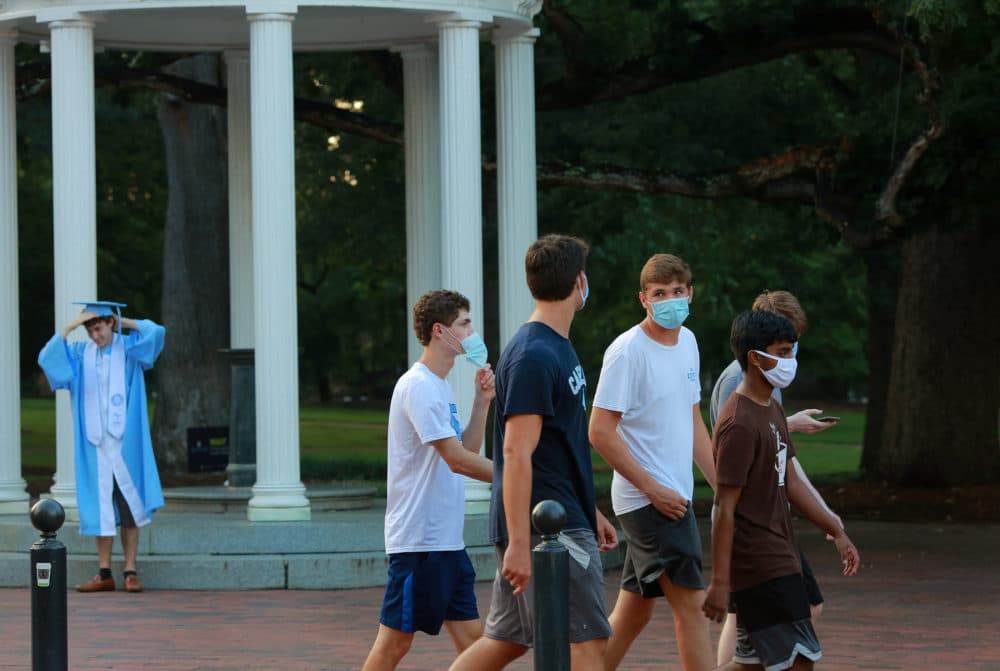 University of North Carolina at Chapel Hill freshmen walk past The Old Well as a recent graduate finishes graduation photos, postponed due to the coronavirus pandemic, on Aug. 8, 2020, in Chapel Hill, NC. (Ted Richardson/Getty Images)