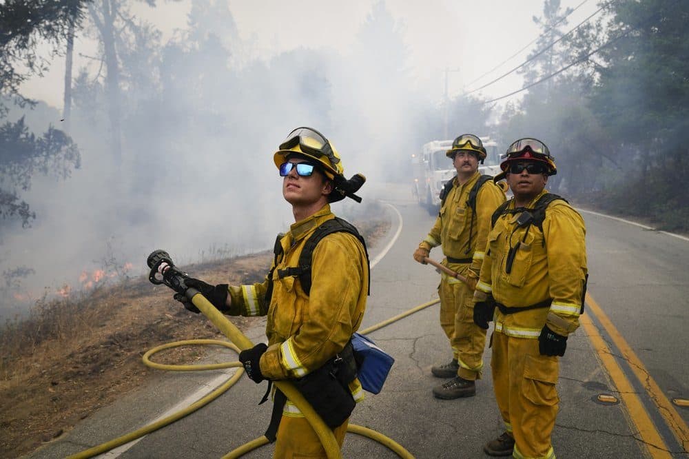 Firefighters Cody Nordstrom, Kyle Harp and Robert Gonzalez, from left, of the North Central Fire station out of Kerman, California, look up at a water-dropping helicopter while fighting the CZU Lightning Complex Fire on Sunday. (Marcio Jose Sanchez/AP)